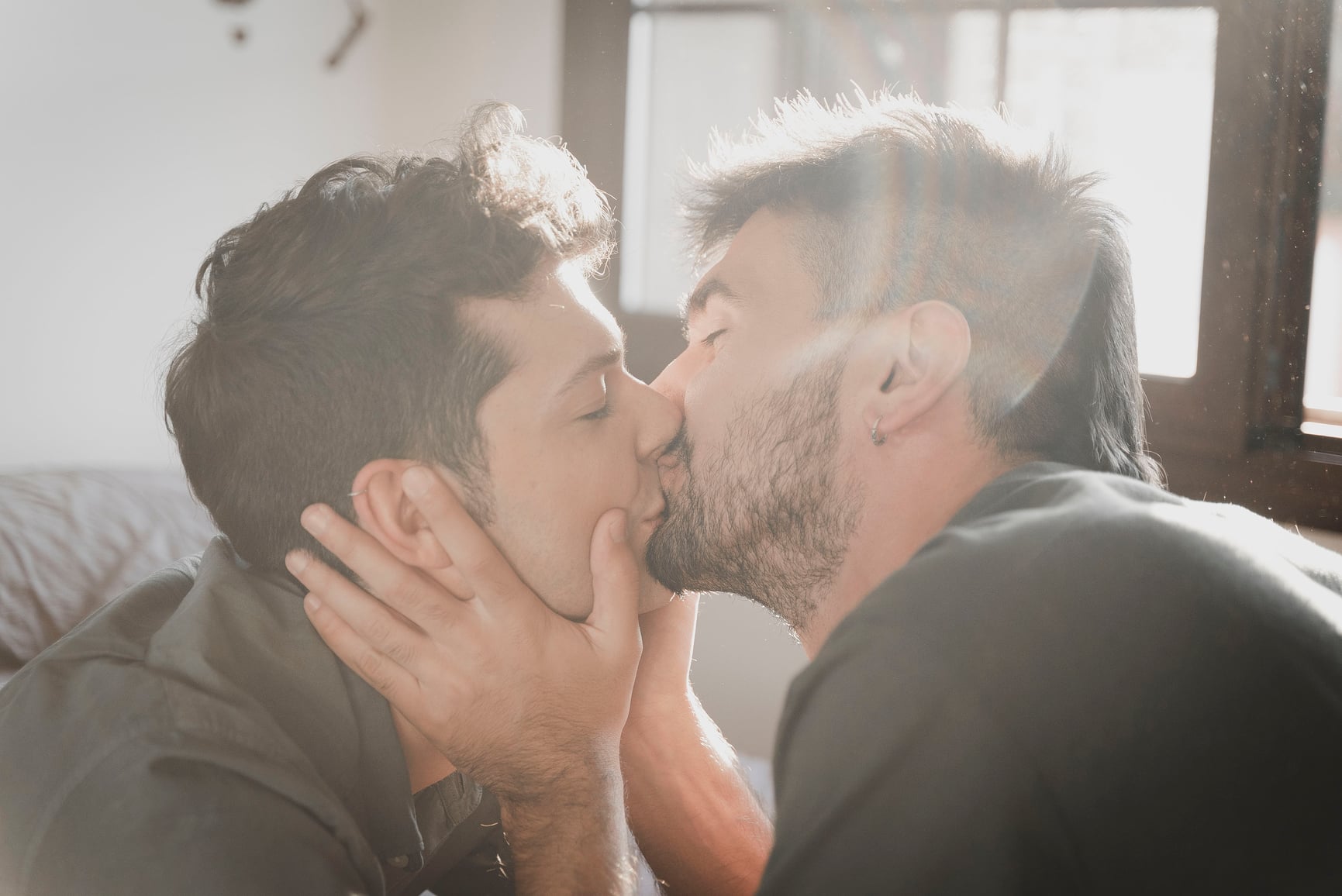 Two men holding each other kissing with bright lighting.