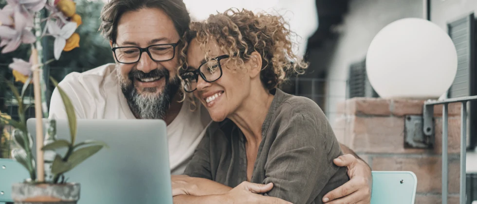 Couple hugging eatch other while watching something on their laptop.