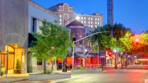 A street in downtown Modesto, lined with buildings and trees. traffic lights.