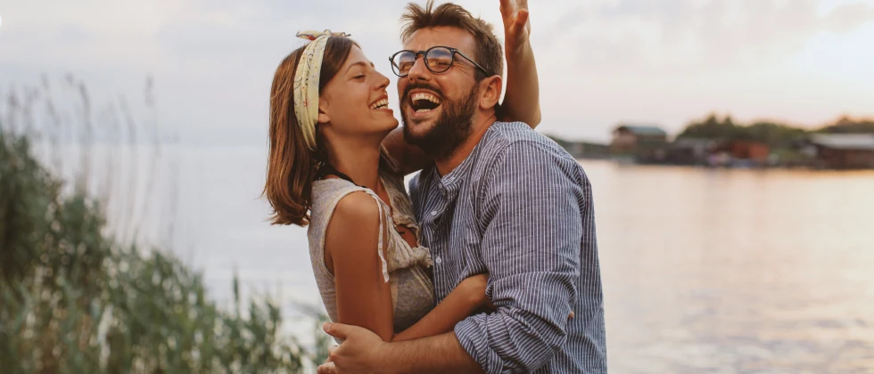 A couple hugging at the lake, and smiling.